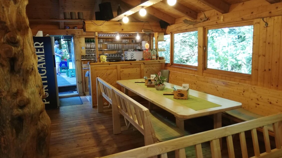 Ein gemütlicher Raum mit Holzwänden und einem großen Tisch. Helle Fenster lassen viel Licht hereinvordern.