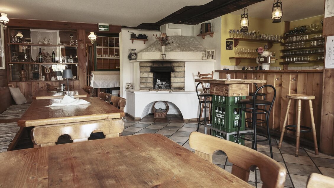 Eine gemütliche Innenansicht eines Restaurants mit Holztischen und Stühlen. Im Hintergrund befindet sich eine Bar und ein Kamin. | © Anton Muchitsch