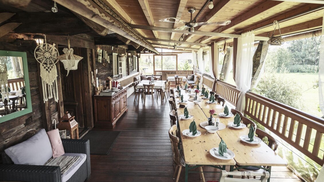 Ein gemütlicher Essbereich mit Holzmöbeln und einem langen Tisch, der dekoriert ist. Große Fenster bieten einen schönen Blick ins Freie. | © Anton Muchitsch