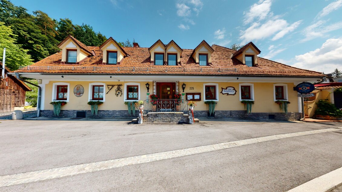 Ein traditionelles Gasthaus mit einem charmanten, reizvollen Design. Die Fassade ist gelb und hat ein rotes Dach, umgeben von einer ruhigen Landschaft. | © Zur Schmied'n - 3D Blick