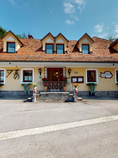 Ein traditionelles Gasthaus mit einem charmanten, reizvollen Design. Die Fassade ist gelb und hat ein rotes Dach, umgeben von einer ruhigen Landschaft. | © Zur Schmied'n - 3D Blick