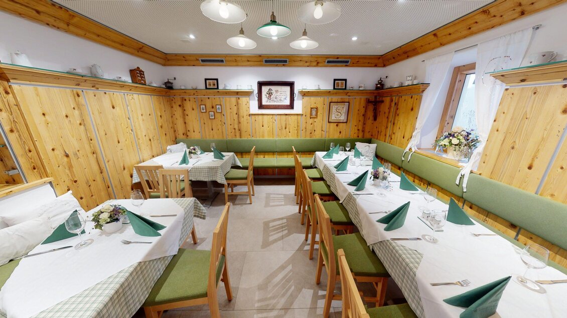 Ein gemütliches Restaurant mit Holzwänden und grünem Mobiliar. Die Tische sind festlich gedeckt und bieten Platz für mehrere Gäste. | © Zur Schmied'n - 3D Blick