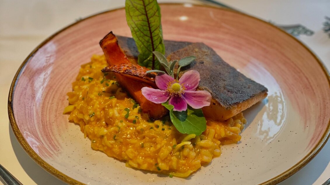 Cremiges Kürbisrisotto mit Fischfilet, Gemüse und Blütendekor auf einem Teller | © Zur Schmied'n