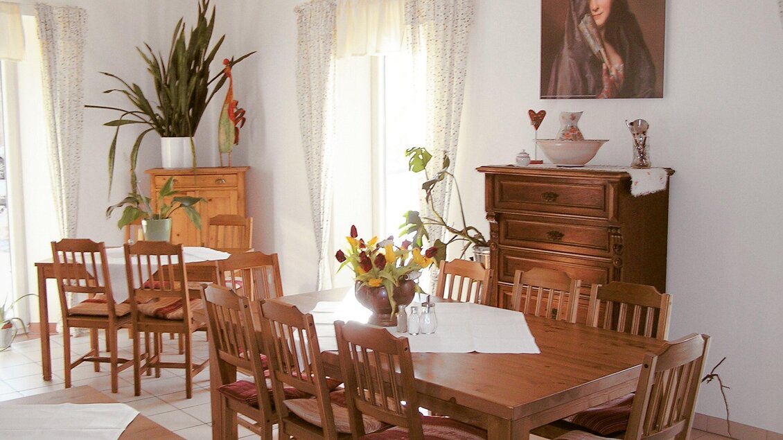 Ein einladender Essbereich mit einem großen Holztisch und Stühlen. Im Hintergrund sind Pflanzen und ein Gemälde zu sehen, die dem Raum eine warme Atmosphäre verleihen. | © Steirerstub'n