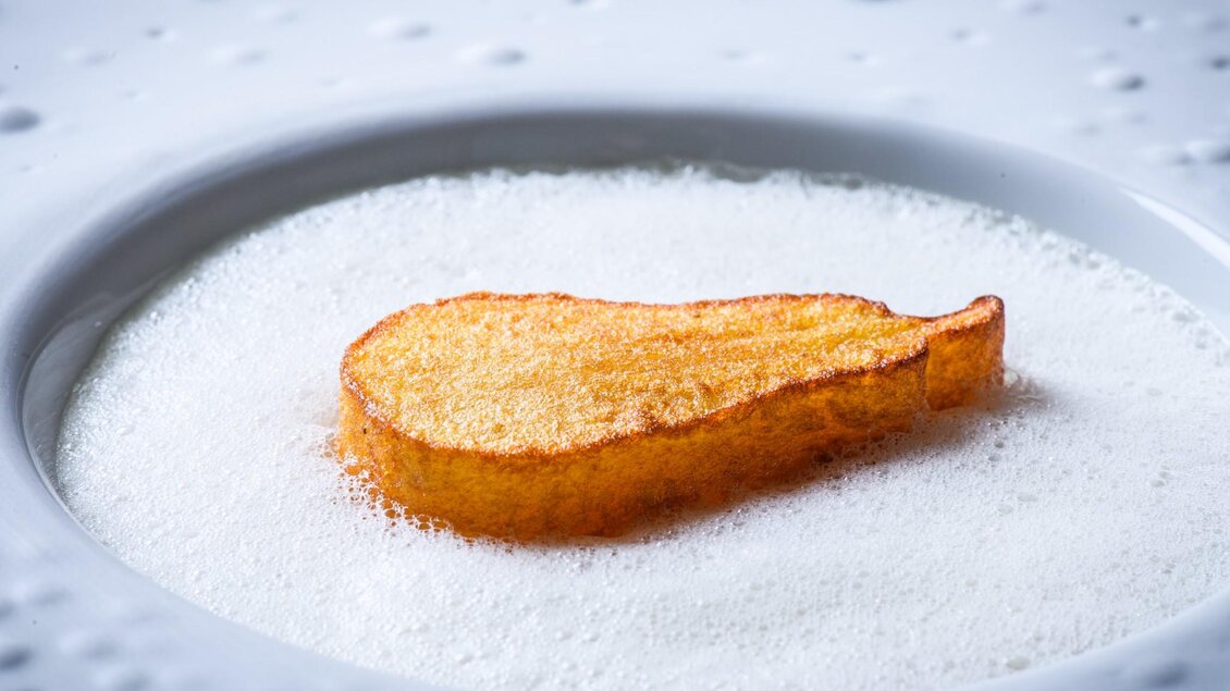 Goldene, birnenförmige Komponente auf weißem Schaum in strukturiertem Porzellanteller. | © Zur goldenen Birn - Jürgen Schmücking