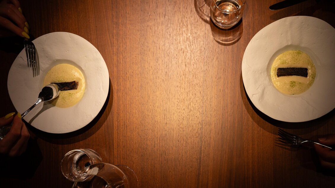 Zwei identisch angerichtete Teller mit Fisch und Sauce an einem Holztisch im Restaurant | © 5komma5sinne - Rene Strasser Fotografie