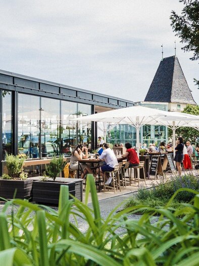 A modern restaurant with a cozy terrace. Guests enjoy the atmosphere outside under a sun umbrella. | © aiola