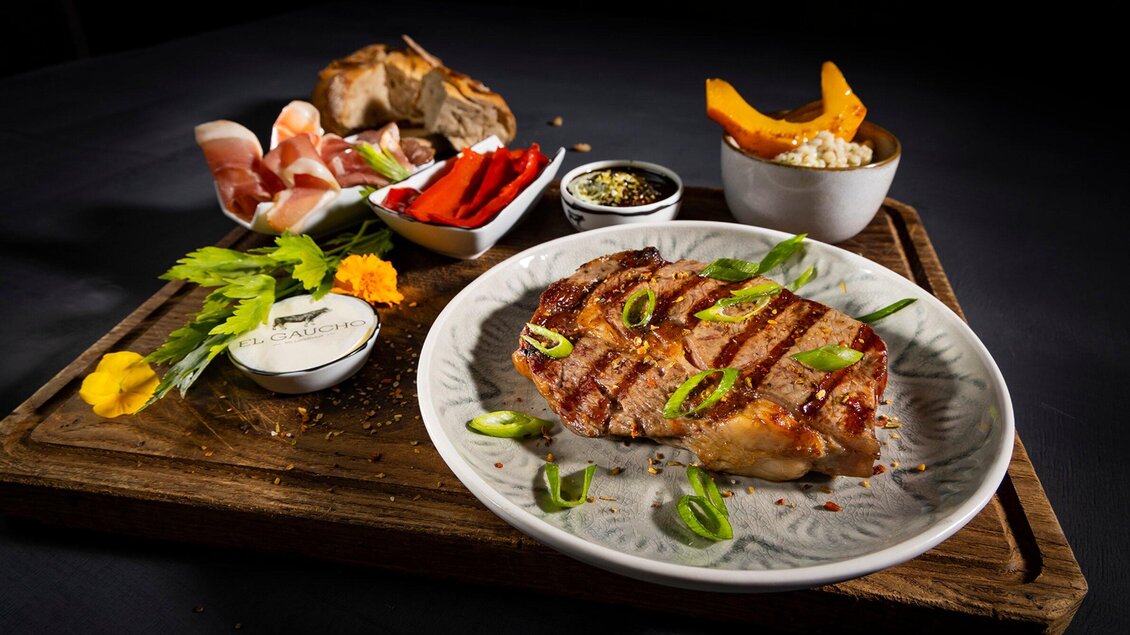 Ein leckerer Teller mit gegrilltem Steak, garniert mit Frühlingszwiebeln. Dazu gibt es eine Auswahl an Beilagen und Dips in kleinen Schüsseln. | © El Gaucho - Werner Krug