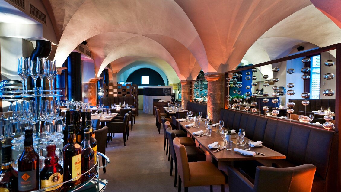 Ein stilvolles Restaurant mit eleganten Tischen und einem Kreuzgewölbe. Die Atmosphäre ist modern und einladend, mit beleuchtetem Barbereich im Vordergrund. | © El Gaucho - Werner Krug