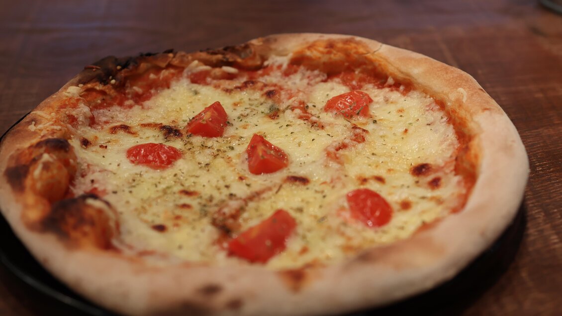 Eine frische Pizza mit geschmolzenem Käse und Tomatenstücken. Der Rand ist goldbraun und knusprig. | © kAlps Foodbar