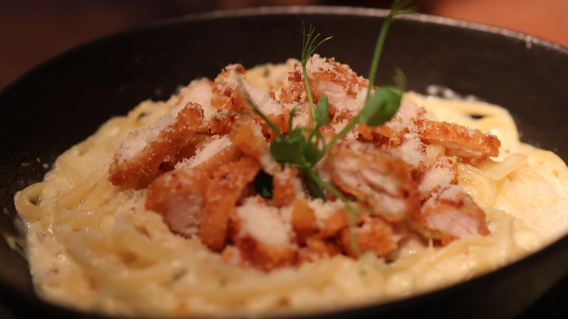 Ein Teller Pasta mit knusprigem Fleisch, überzogen mit Käse und frischen Kräutern. Das Gericht sieht lecker und einladend aus. | © kAlps Foodbar