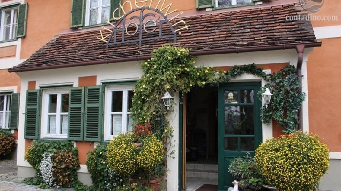 Ein charmantes Gebäude mit einer blühenden Fassade und grünen Fensterläden. Die Eingangstür ist einladend und durch Pflanzen geschmückt. | © Kirchenwirt Hofer