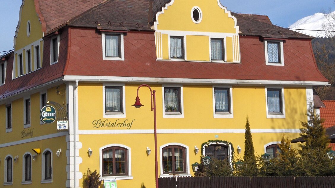 Ein gelb gestrichenes Gebäude mit roten Dächern und weißen Fenstern. Es handelt sich um ein Gasthaus mit einem einladenden Außenbereich. | © Gasthof Pölstalerhof