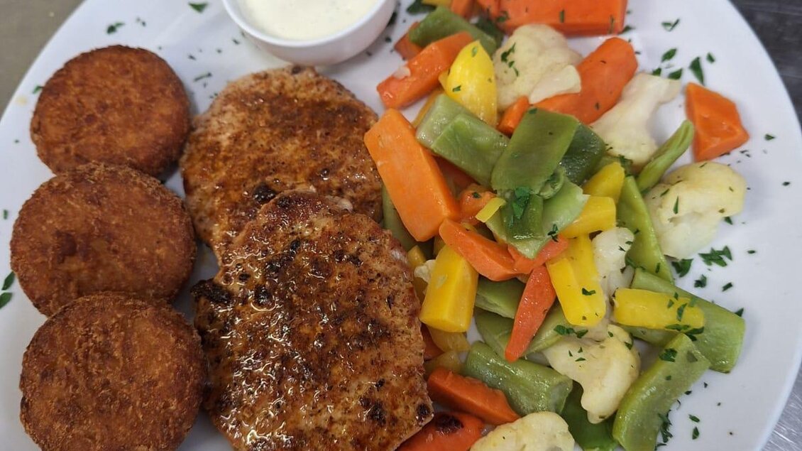 Ein Teller mit gebratenen Frikadellen, frittierten Kartoffelröllchen und einer bunten Gemüsemischung. Dazu gibt es eine Schale mit Sauerkraut. | © Gasthof Pölstalerhof