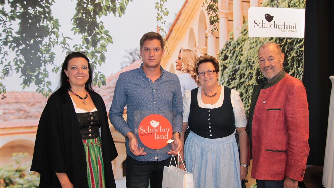 Eine Gruppe von vier Personen steht vor einer attraktiven Kulisse mit einem Banner für "Schluchterland". Die Personen sind freundlich und festlich gekleidet. | © Netwerker Mediahaus