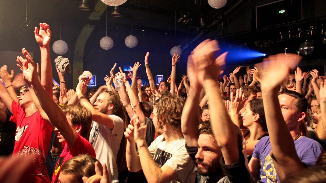 Eine begeisterte Menschenmenge hebt die Hände und tanzt in einem Konzertsaal. Die Atmosphäre ist lebhaft und energiegeladen. | © ppc