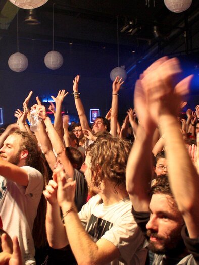 An enthusiastic crowd raises their hands and dances in a concert hall. The atmosphere is lively and energetic. | © ppc