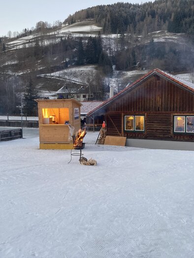 Ein gemütliches Holzhaus in einer verschneiten Landschaft. Im Vordergrund stehen Fackeln und die Umgebung ist von Bäumen und Hügeln umgeben. | © Jürgen Strohmeyer