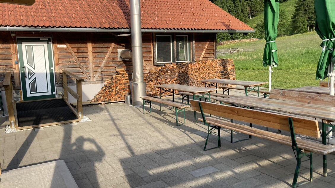Eine Terrasse mit Holztischen und Bänken. Im Hintergrund ist ein schönes Holzhaus und die grüne Landschaft zu sehen. | © Jürgen Strohmeyer