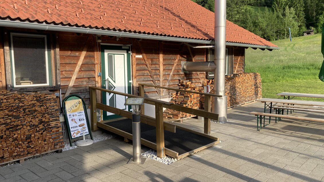 Ein gemütliches Holzhaus mit einem roten Dach. Draußen stehen einige Tische und Bänke sowie gestapelte Holzscheite. | © Jürgen Strohmeyer