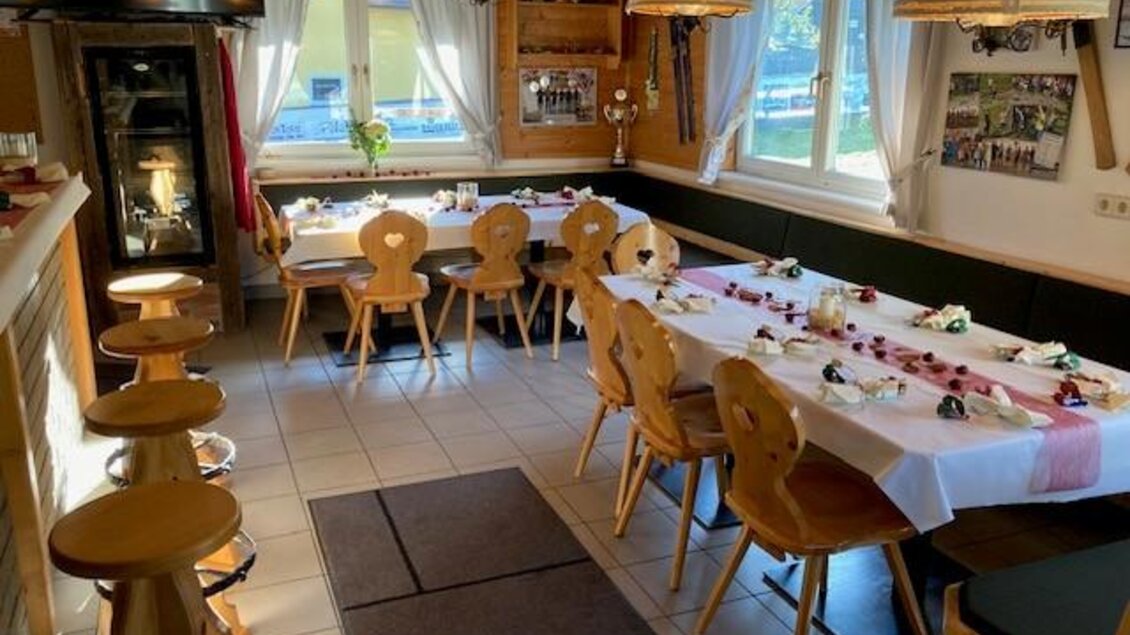 Ein gemütlicher Gastraum mit holzernen Möbeln und festlich gedeckten Tischen. Durch die Fenster strömt Tageslicht in den Raum. | © Jürgen Strohmeyer