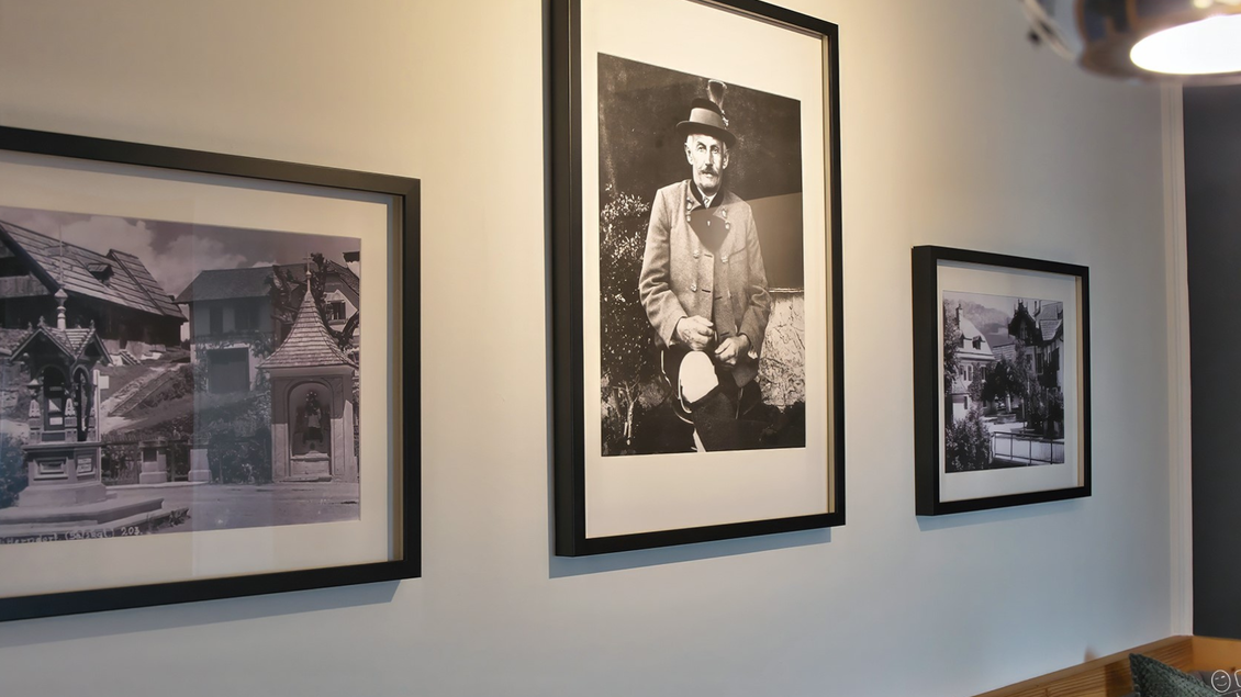 Drei gerahmte Schwarz-Weiß-Fotos hängen an einer hellen Wand. Die Bilder zeigen alte Architektur und eine Person in traditioneller Kleidung. | © event-fotograf.at