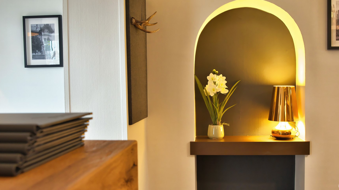 Ein stilvoller Raum mit einem holzfarbenen Tisch, einem eleganten Lampen und frischen Blumen in der Nische. Die Wände sind hell und mit Bildern dekoriert. | © event-fotograf.at