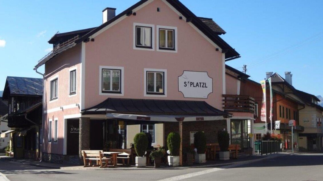 Ein charmantes Gebäude in einer kleinen Stadt mit einem Schild "5° Platz". Es gibt Tische und Stühle im Freien und eine klare, blaue Himmel. | © S´Platzl