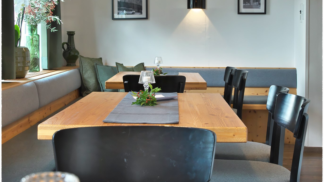 Ein gemütlicher Restaurantbereich mit Holzstühlen und Tischen. Die Wände sind dekoriert mit Bildern und eine grüne Pflanze verleiht der Atmosphäre Frische. | © event-fotograf.at