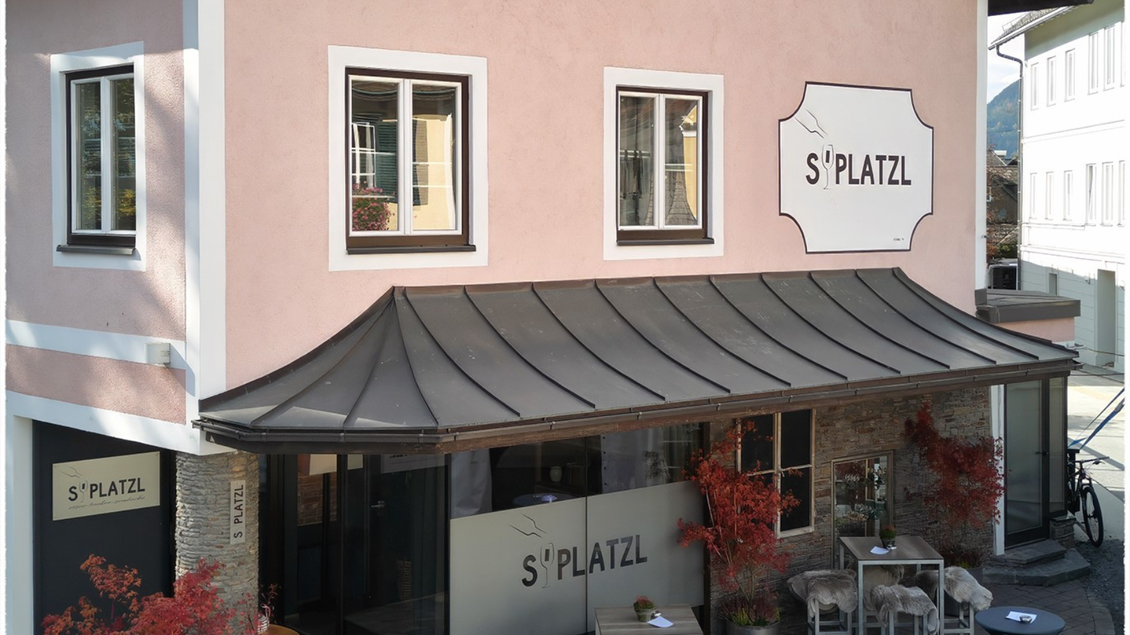 Ein modernes Gebäude mit einem einladenden Außenbereich. Der Schriftzug "S'PLATZL" ist gut sichtbar und zieht die Aufmerksamkeit auf sich. | © event-fotograf.at
