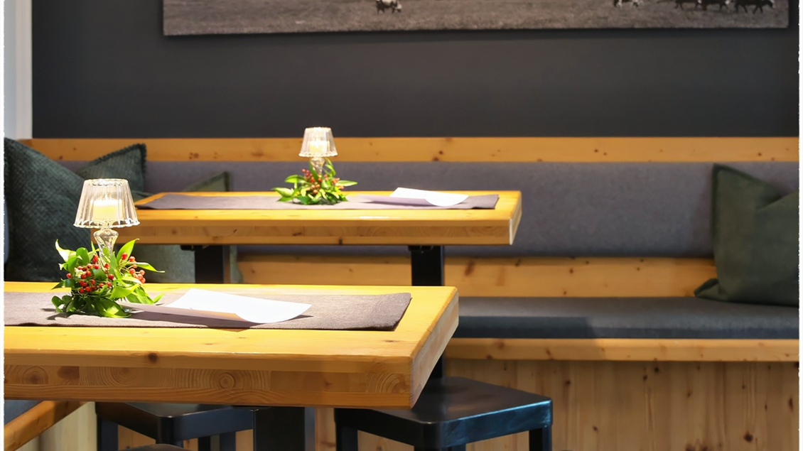 Ein gemütlicher Essbereich mit Holztischen und einer Sitzbank. Auf den Tischen stehen kleine Pflanzenarrangements und Kerzen. | © event-fotograf.at