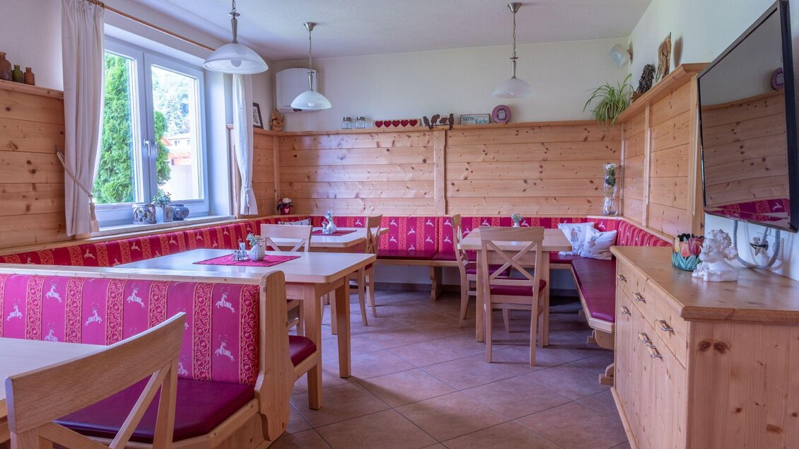 Ein gemütlicher Essbereich mit Holzmöbeln und rot-rosafarbenen Sitzpolstern. Große Fenster sorgen für viel Tageslicht. | © s'Wirtshaus