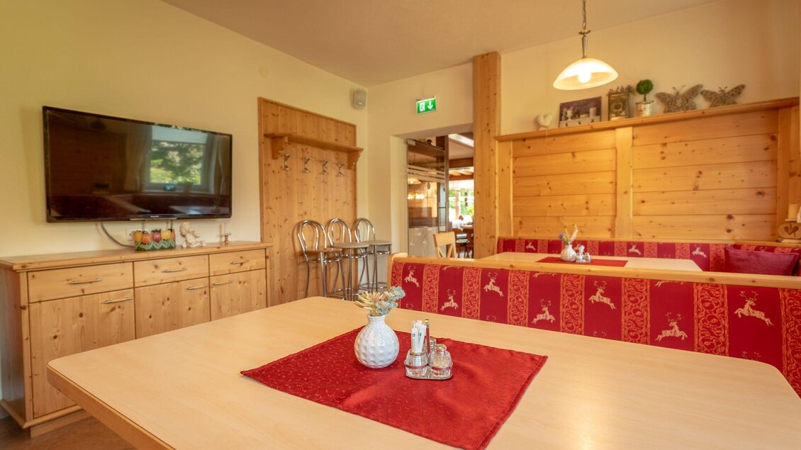 Ein helles und gemütliches Esszimmer mit Holzmöbeln. Es gibt einen großen Tisch, eine Fernsehecke und eine einladende Sitzbank. | © s'Wirtshaus