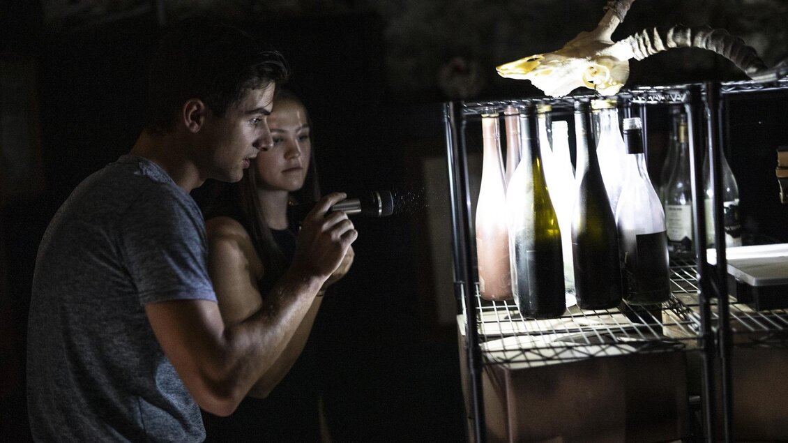 Zwei Personen betrachten aufmerksam Flaschen auf einem Regal. Im Hintergrund ist ein Tier sichtbar, das auf dem Regal sitzt. | © Apolla GmbH