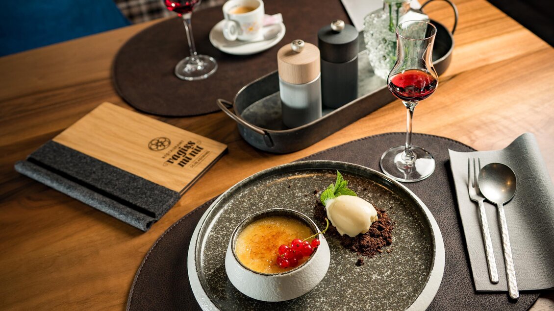 Das Bild zeigt ein Dessert mit Creme brûlée, Eis und roten Johannisbeeren, dazu ein Glas Likör und eine Tasse Kaffee auf einem gedeckten Tisch. | © Vagiss mi nit