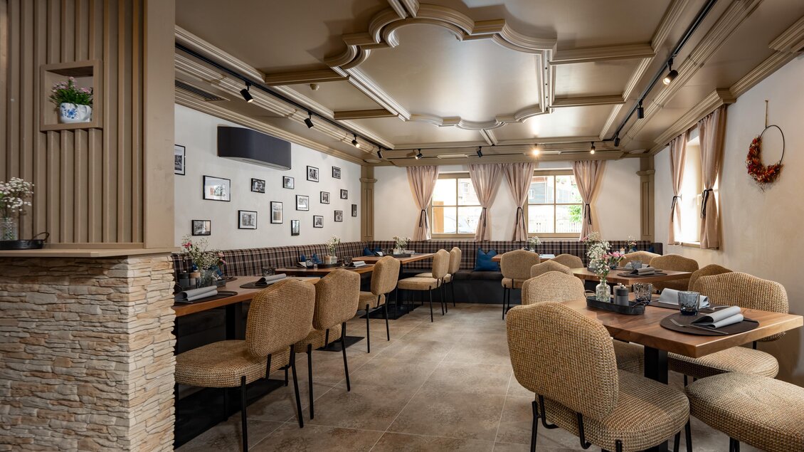 Gemütlicher, stilvoll eingerichteter Gastraum mit Holztischen, gepolsterten Stühlen, dekorativen Bildern an den Wänden und viel Tageslicht durch große Fenster | © Vagiss mi nit