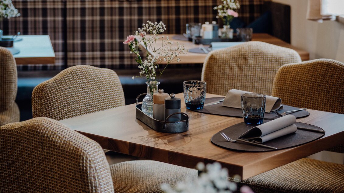 Gemütlicher Gastraum mit Holztischen, gepolsterten Stühlen und kleinen Blumendekorationen auf den Tischen. | © Vagiss mi nit