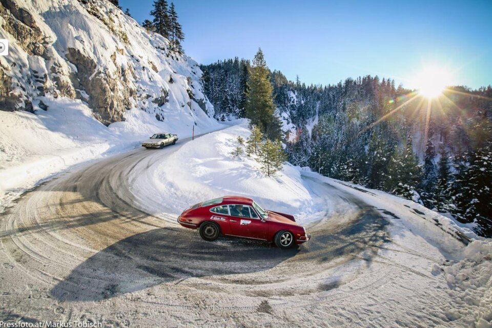 Zwei Autos fahren in einer schneebedeckten Berglandschaft. Die Sonne scheint durch die Bäume und lässt die Szene strahlend erscheinen. | © Markus Tobisch