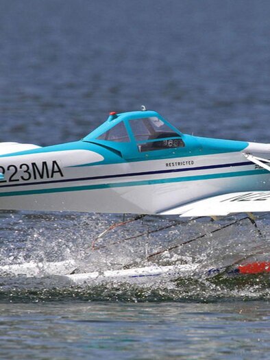 A seaplane takes off from the surface of a lake. It splashes water and has a striking blue and white paint job. | © Ian Walter