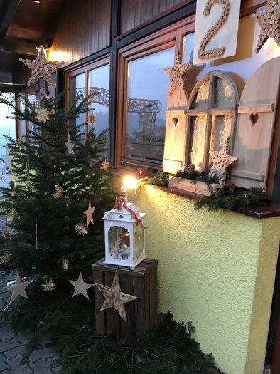 A festively decorated entrance area with a Christmas tree, stars, and a lantern. The walls are adorned with Christmas decorations. | © Verein "Wir am Berg"