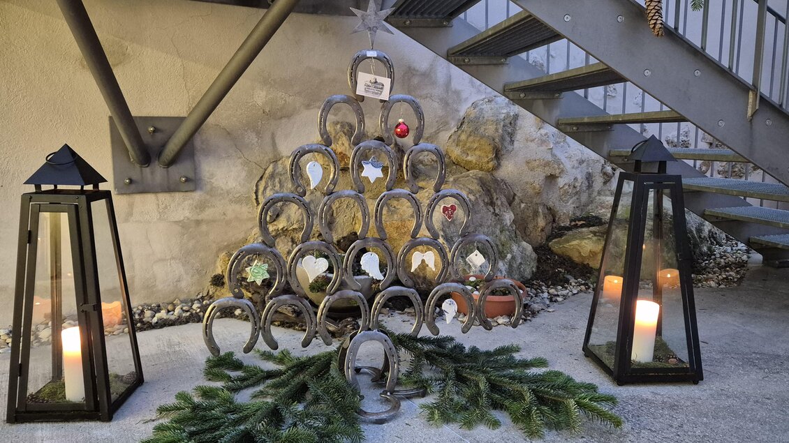 Ein kreativer Weihnachtsbaum aus Hufeisen steht auf dem Boden. Daneben befinden sich zwei laternen mit Kerzen und etwas Tannengrün. | © Oststeiermark Tourismus