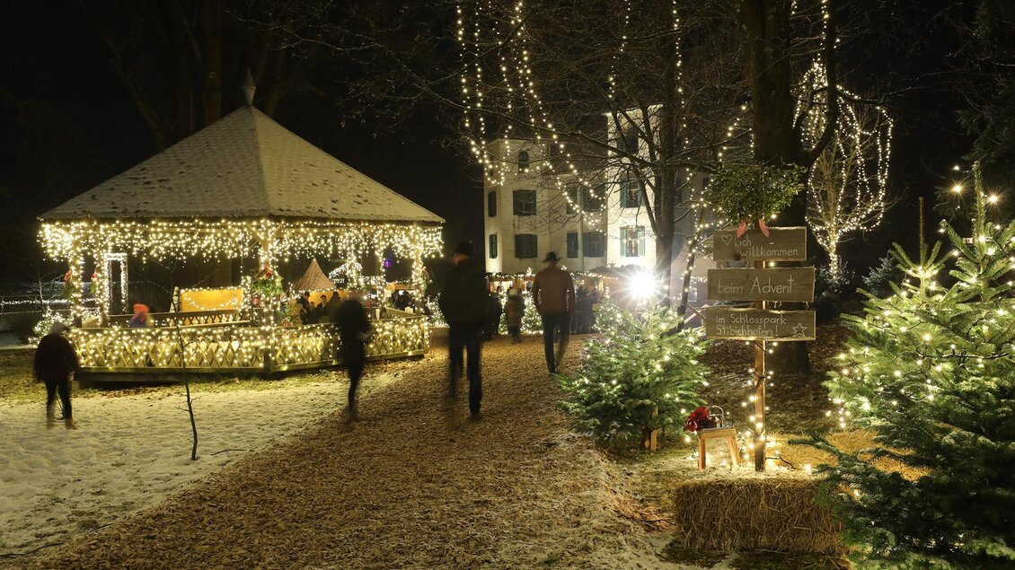 Ein festlich beleuchteter Platz mit einem Pavillon und geschmückten Weihnachtsbäumen. Menschen spazieren durch die verschneite Umgebung in der Nacht. | © Stadtgemeinde Trofaiach