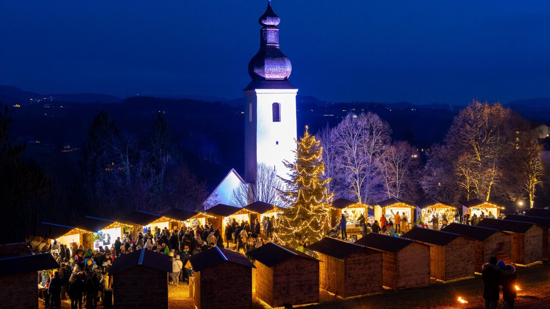 Abendlicher Adventmarkt mit Lichterbaum und Kirche in St. Bartholomä | © Region Graz-Harry Schiffer