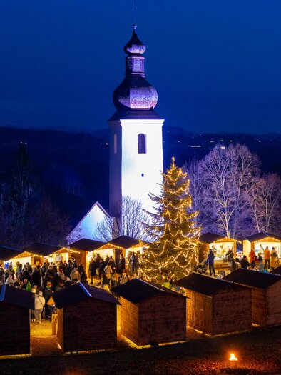 Evening Advent market with light tree and church in St. Bartholomew | © Region Graz-Harry Schiffer