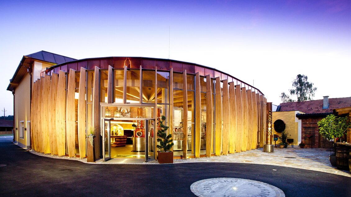 Ein modernes Gebäude mit einer runden Holzfassade im Freien. Der Eingang ist einladend und von grünen Pflanzen umgeben. | © Werner Krug