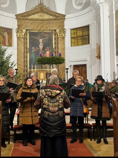 A choir is singing in a church, surrounded by festive decorations. In the background, there is an Advent wreath and Christmas trees. | © Franz-Peter Stadler