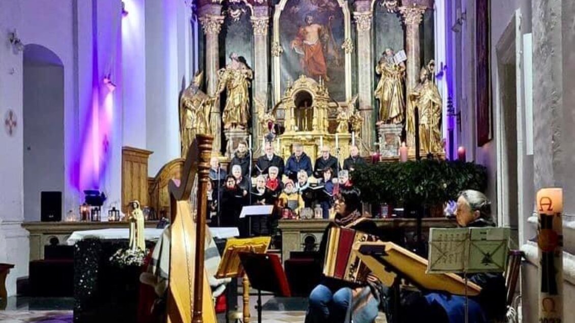 Eine musikalische Aufführung in einer Kirche mit einer Gruppe von Musikern und einem Chor. Der Altar ist prächtig dekoriert und wird von bunten Lichtern beleuchtet. | © Sängerverein Mureck