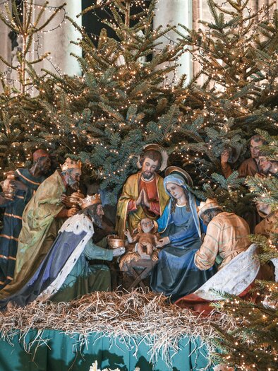 A nativity scene with the Holy Family, surrounded by fir trees and lights. The scene conveys a festive atmosphere for Christmas. | © mustafa-turhan-unsplash