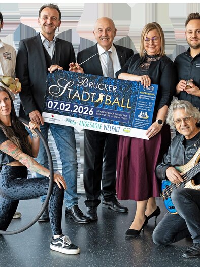 A group of six people poses together while holding a poster for the Brucker City Ball. The ball will take place on February 7, 2026. | © Rotes Kreuz - Tamara Kury