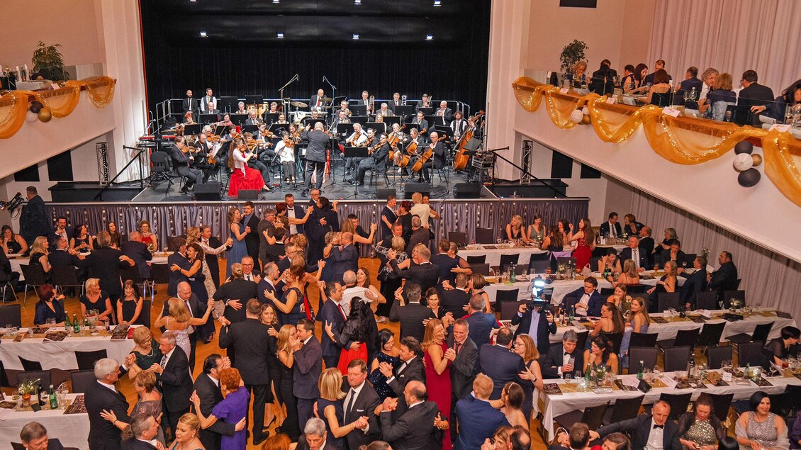 Eine festliche Veranstaltung mit vielen Gästen, die tanzen und feiern. Im Hintergrund spielt ein Orchester auf einer Bühne. | © Ekaterina Paller